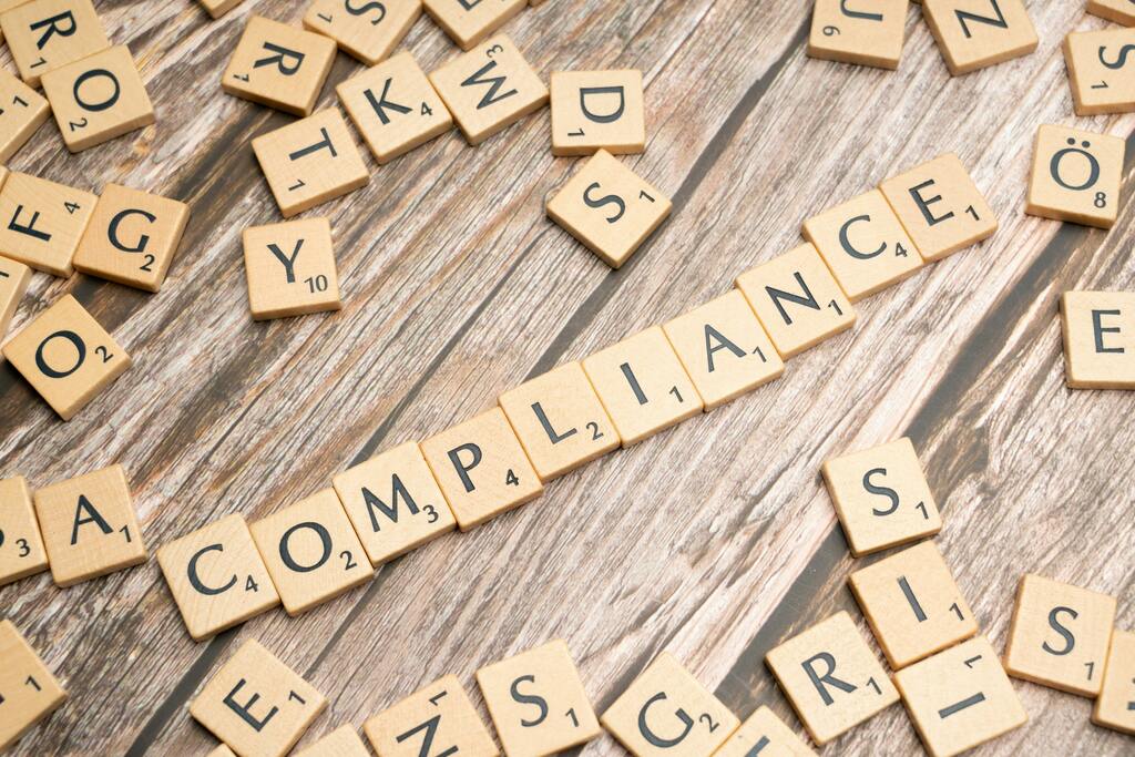 The word compliance spelled in letter tiles